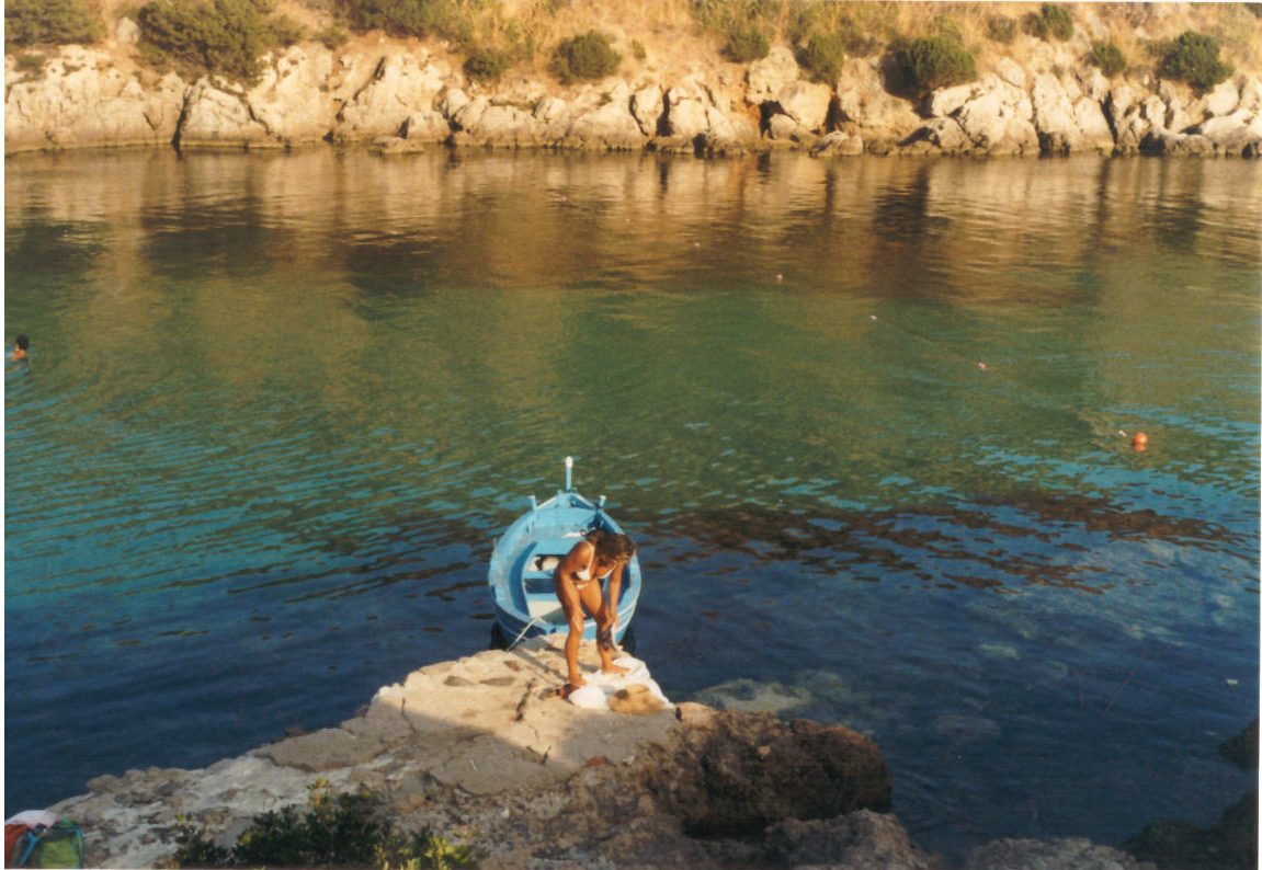Fotografia su pellicola: una persona seduta sugli scogli in riva all'acqua, Sardegna